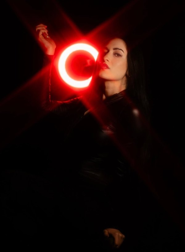 Crystal Mia in profile with one hand raised beside a glowing red ring